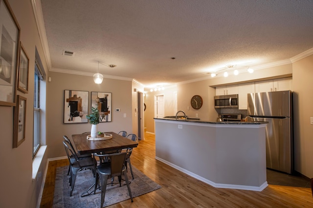 dining space featuring ornamental molding, a textured ceiling, and light wood-type flooring