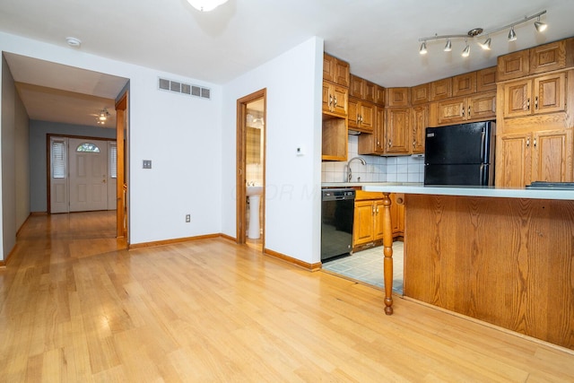 kitchen with black appliances, light wood-type flooring, sink, and tasteful backsplash