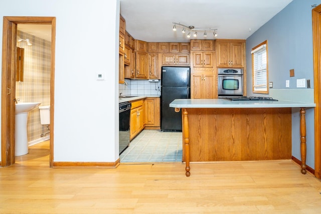 kitchen featuring black appliances, sink, decorative backsplash, light wood-type flooring, and kitchen peninsula