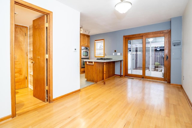 kitchen featuring light wood-type flooring, kitchen peninsula, and stainless steel double oven