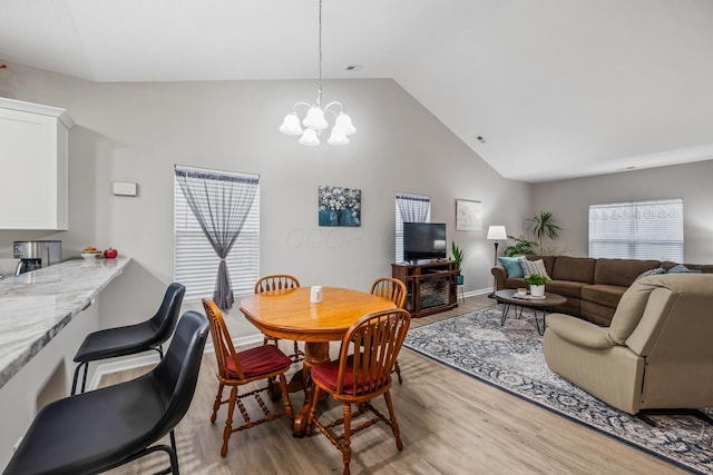 dining room with an inviting chandelier, high vaulted ceiling, and light hardwood / wood-style flooring