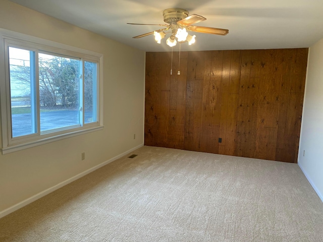 unfurnished room featuring carpet floors, wooden walls, and ceiling fan