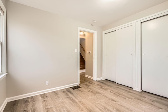 unfurnished bedroom with light wood-type flooring and multiple closets