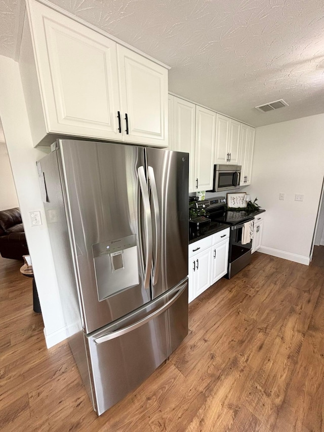 kitchen featuring white cabinetry, stainless steel appliances, a textured ceiling, and wood-type flooring