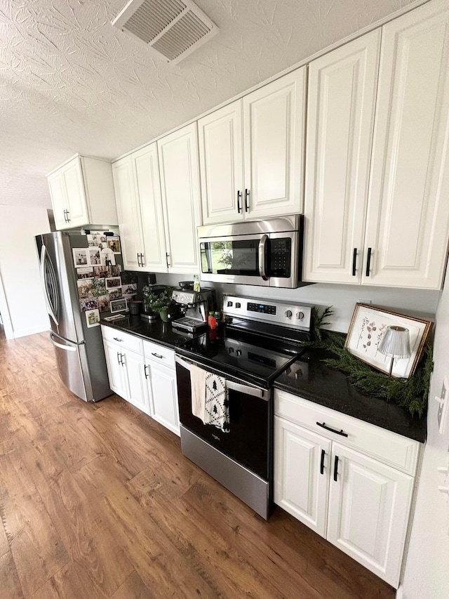 kitchen featuring hardwood / wood-style floors, white cabinets, a textured ceiling, and appliances with stainless steel finishes