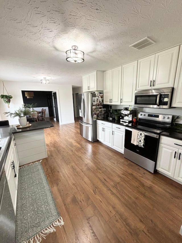 kitchen featuring kitchen peninsula, a textured ceiling, stainless steel appliances, dark wood-type flooring, and white cabinetry