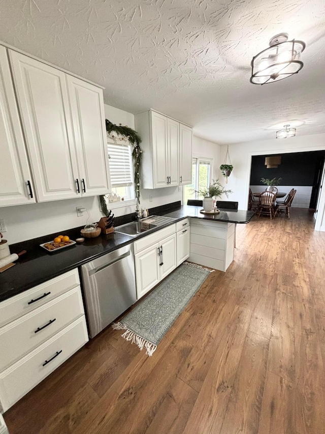 kitchen with kitchen peninsula, wood-type flooring, white cabinetry, and stainless steel dishwasher