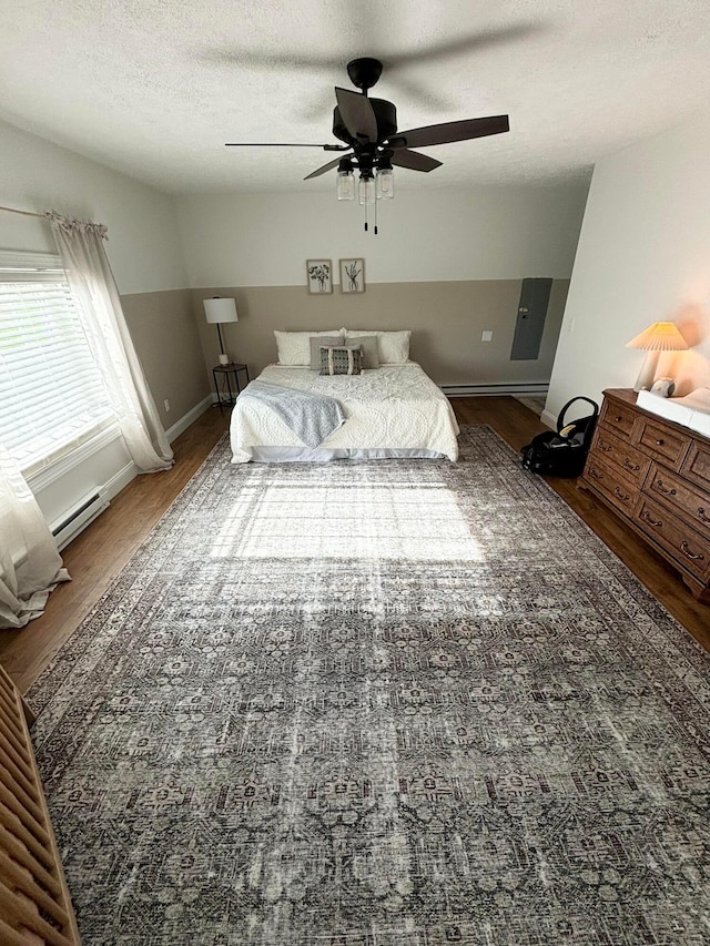 bedroom with hardwood / wood-style floors, ceiling fan, a textured ceiling, and a baseboard heating unit