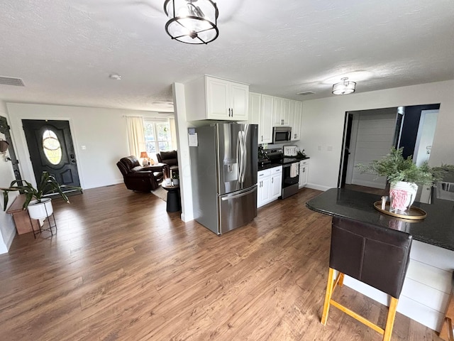 kitchen with hardwood / wood-style floors, a textured ceiling, stainless steel appliances, and white cabinetry