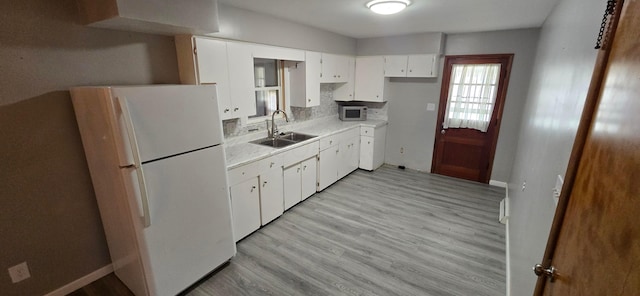 kitchen with backsplash, white cabinets, white refrigerator, sink, and light wood-type flooring