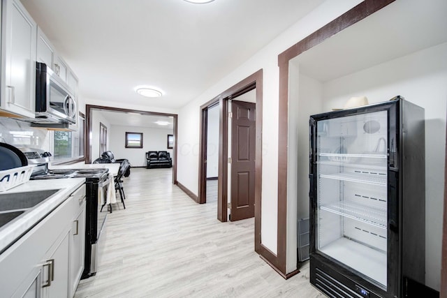 kitchen with range with electric cooktop, white cabinets, light hardwood / wood-style floors, and beverage cooler