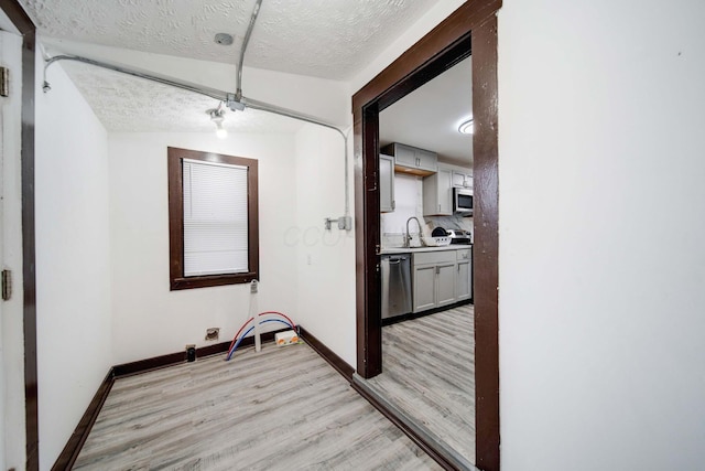 corridor featuring a textured ceiling, light hardwood / wood-style flooring, lofted ceiling, and sink