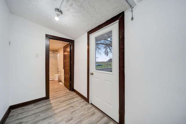 hallway with light wood-type flooring, lofted ceiling, and a textured ceiling