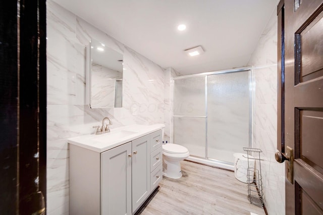 bathroom with vanity, a shower with door, wood-type flooring, tile walls, and toilet