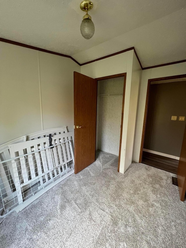 unfurnished bedroom featuring lofted ceiling, ornamental molding, a textured ceiling, carpet floors, and a closet