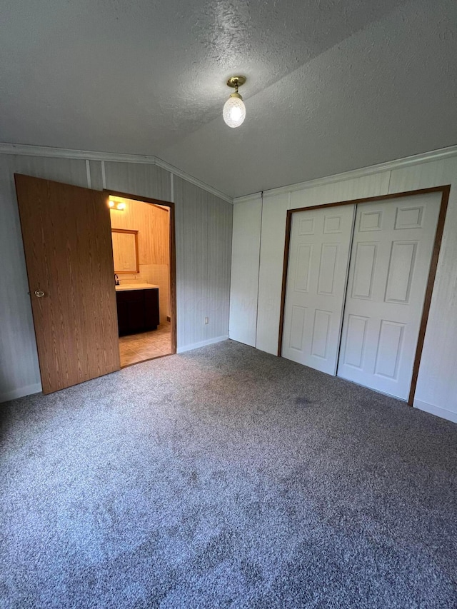 unfurnished bedroom with connected bathroom, carpet floors, a textured ceiling, vaulted ceiling, and a closet