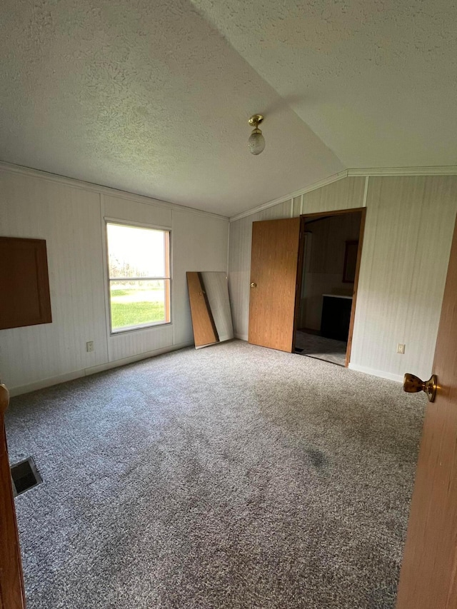 unfurnished living room featuring carpet flooring, lofted ceiling, a textured ceiling, and wooden walls