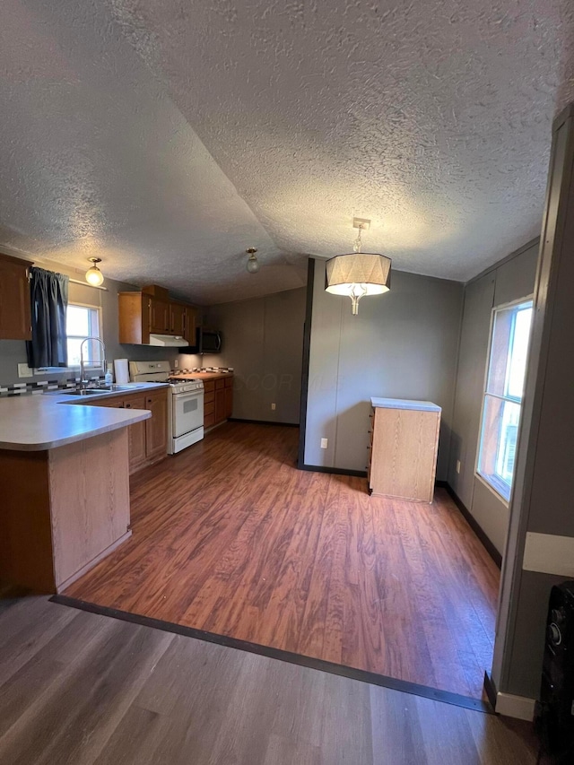 kitchen with a textured ceiling, white range with gas stovetop, kitchen peninsula, and dark wood-type flooring