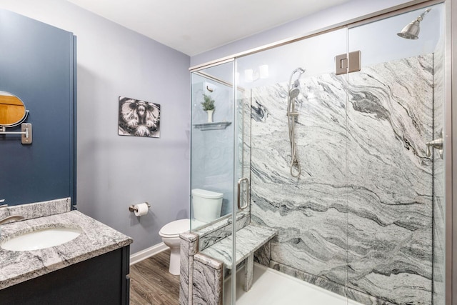 bathroom featuring toilet, wood finished floors, a marble finish shower, baseboards, and vanity