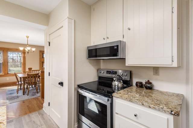 kitchen with light wood-type flooring, light stone counters, appliances with stainless steel finishes, a notable chandelier, and white cabinetry