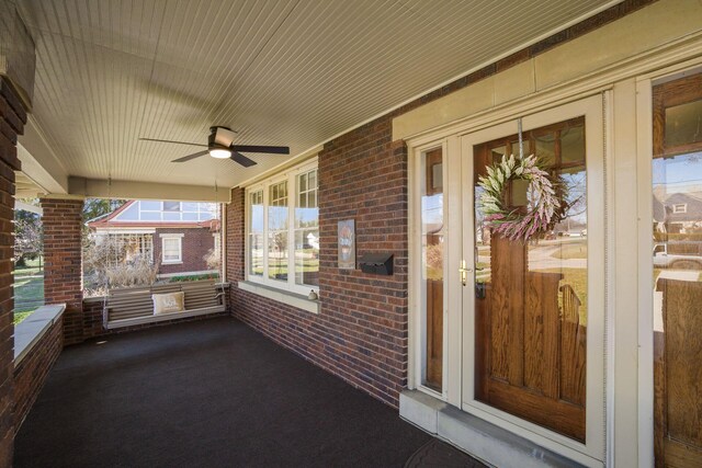 doorway to property featuring brick siding, covered porch, and ceiling fan