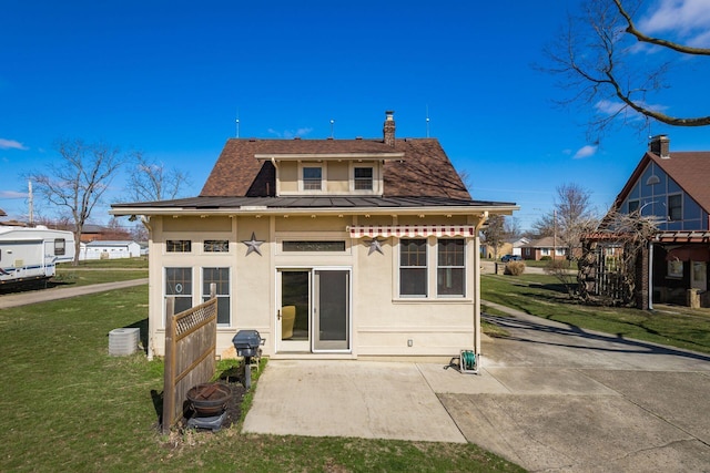 back of property with stucco siding, a patio, a yard, a shingled roof, and a chimney