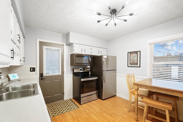 kitchen featuring white cabinets, sink, light wood-type flooring, a textured ceiling, and appliances with stainless steel finishes