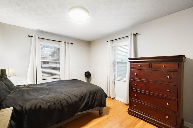 bedroom featuring a textured ceiling, light hardwood / wood-style floors, and multiple windows