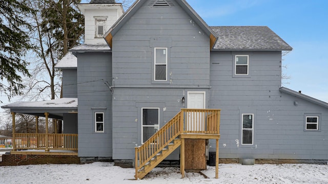 snow covered back of property with a porch and roof with shingles