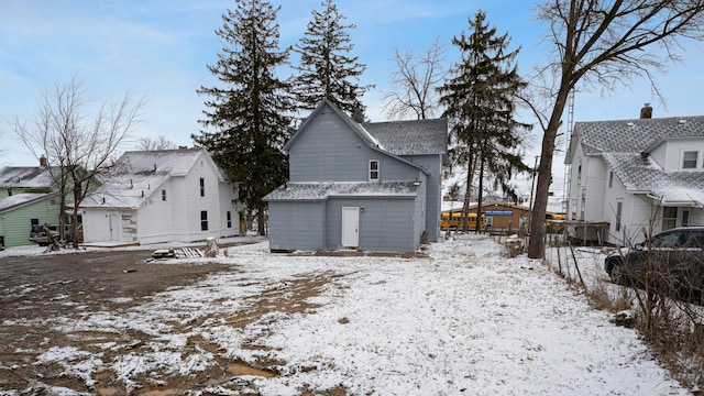 snow covered back of property with roof with shingles and an outbuilding