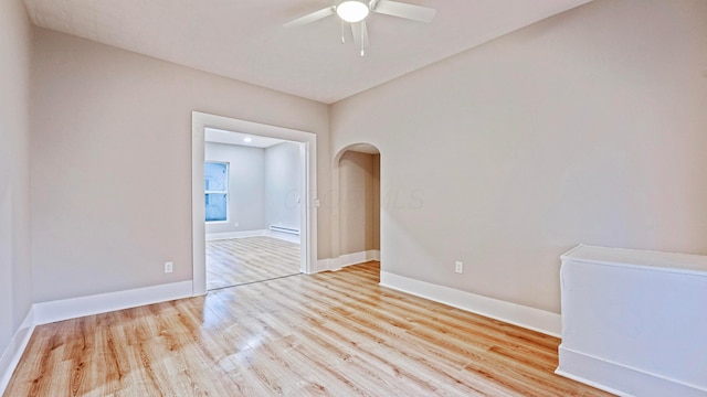 empty room featuring arched walkways, ceiling fan, wood finished floors, and baseboards