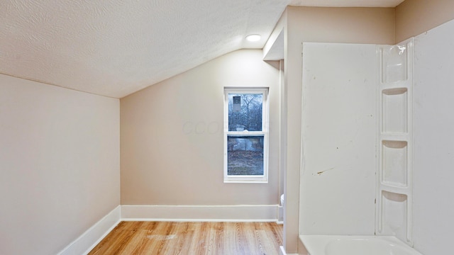 bonus room featuring a textured ceiling, vaulted ceiling, light wood-type flooring, and baseboards