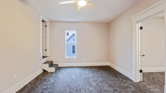 spare room with ceiling fan, baseboards, and dark colored carpet