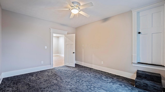 unfurnished bedroom with a ceiling fan, dark colored carpet, and baseboards