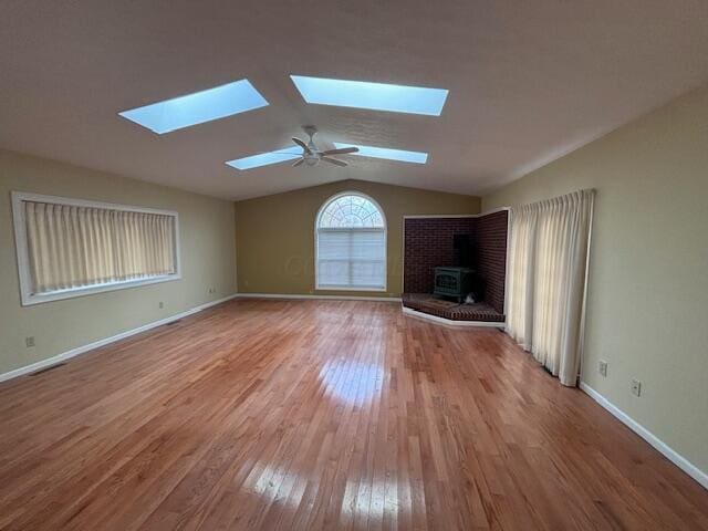 unfurnished living room with a wood stove, ceiling fan, light hardwood / wood-style floors, and lofted ceiling