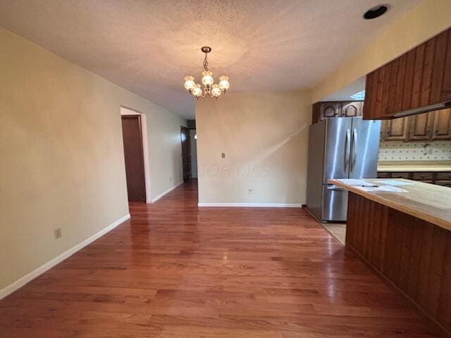 kitchen featuring dark wood-type flooring, an inviting chandelier, backsplash, stainless steel fridge, and decorative light fixtures