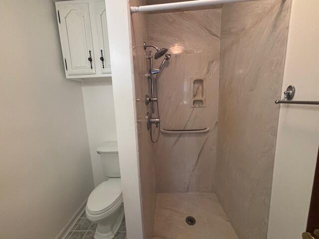 bathroom featuring tile patterned flooring, toilet, and a tile shower