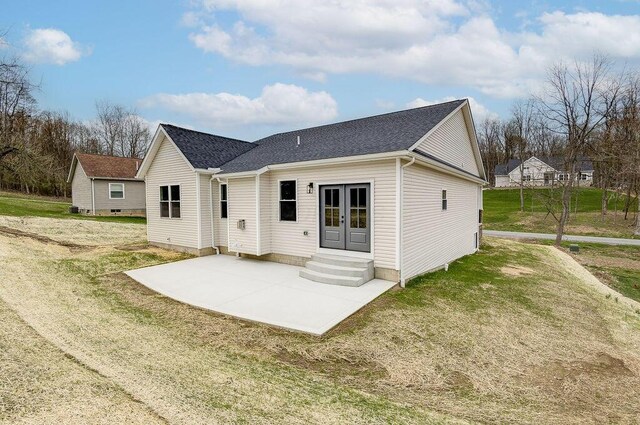 rear view of property with a lawn, french doors, a patio area, entry steps, and a shingled roof