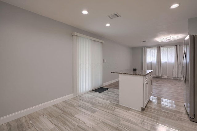 kitchen featuring stainless steel fridge, stone counters, white cabinets, a center island, and light hardwood / wood-style floors