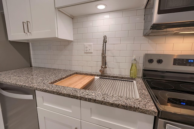 kitchen featuring tasteful backsplash, stainless steel appliances, sink, dark stone countertops, and white cabinetry