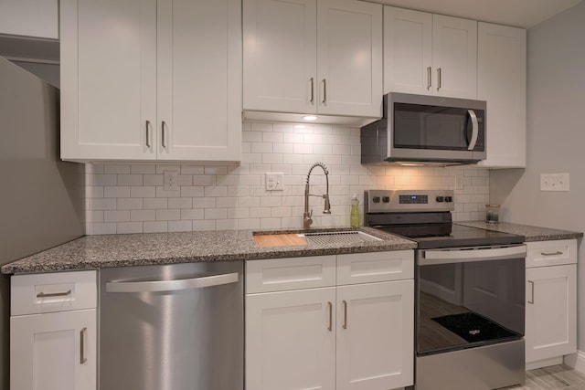 kitchen with sink, appliances with stainless steel finishes, tasteful backsplash, light stone counters, and white cabinetry