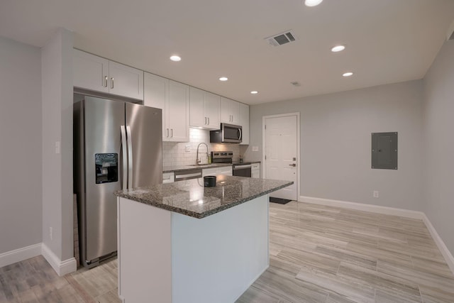 kitchen featuring appliances with stainless steel finishes, tasteful backsplash, dark stone countertops, white cabinets, and a center island