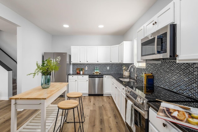 kitchen featuring appliances with stainless steel finishes, light wood-type flooring, tasteful backsplash, sink, and white cabinetry