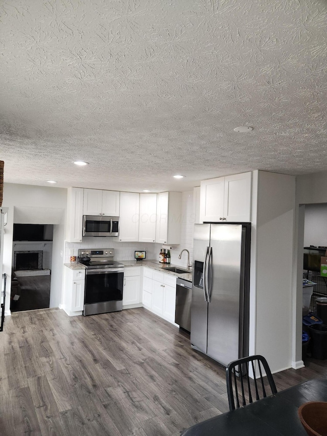 kitchen with appliances with stainless steel finishes, backsplash, dark wood-type flooring, sink, and white cabinetry