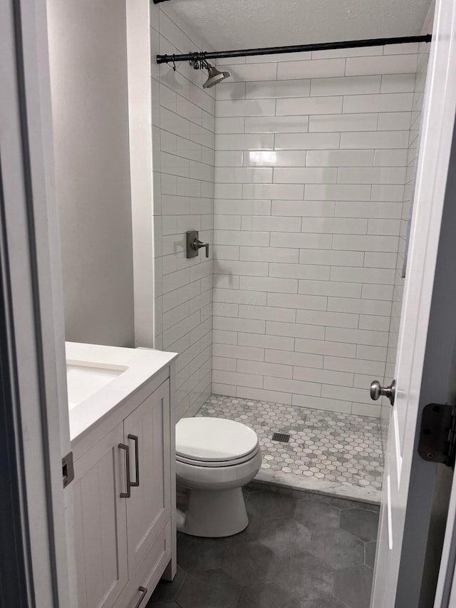 bathroom featuring tiled shower, vanity, a textured ceiling, and toilet