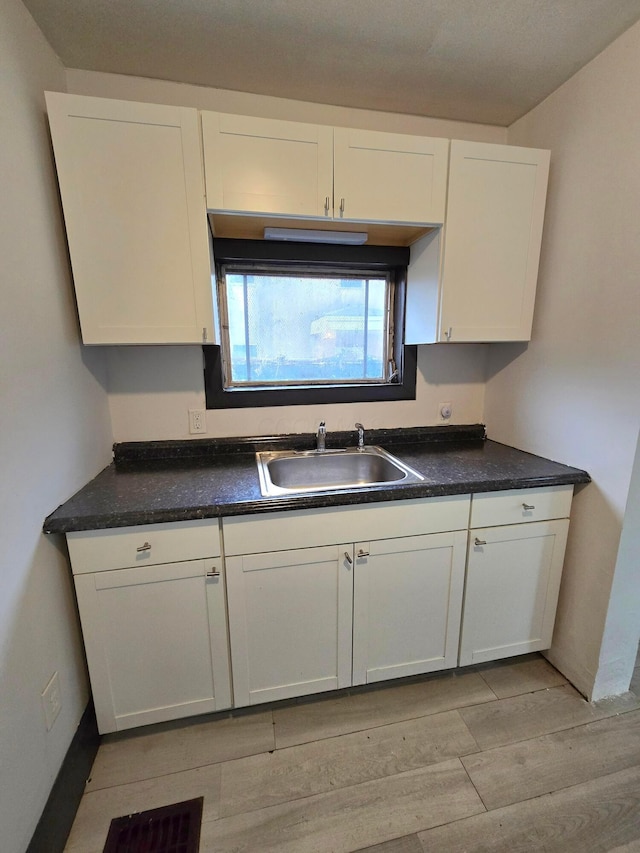 kitchen with white cabinets, light wood-type flooring, and sink