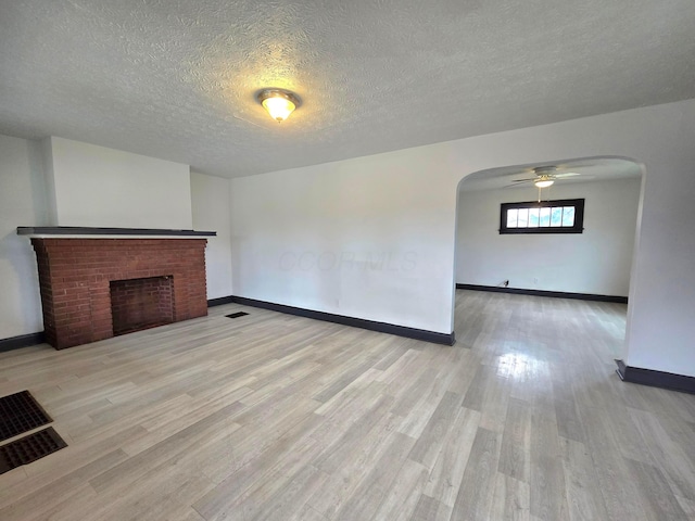 unfurnished living room with ceiling fan, light hardwood / wood-style floors, a textured ceiling, and a brick fireplace