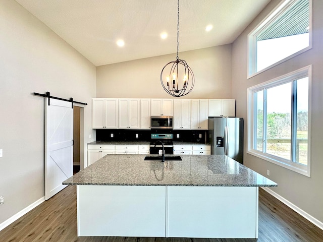 kitchen with a barn door, stone counters, pendant lighting, and stainless steel appliances