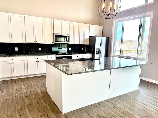 kitchen with appliances with stainless steel finishes, sink, pendant lighting, white cabinets, and an island with sink