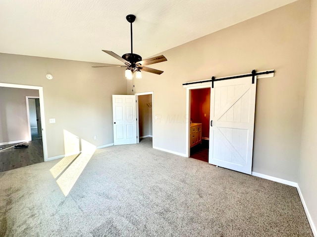 unfurnished bedroom with carpet flooring, ensuite bathroom, a textured ceiling, ceiling fan, and a barn door